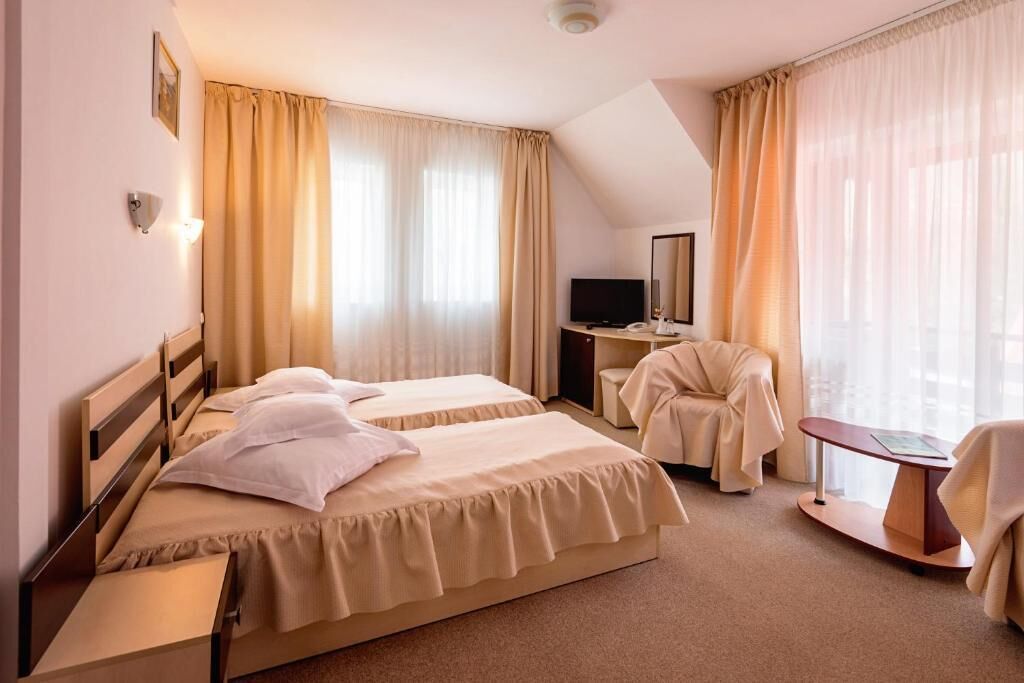 Habitación de hotel con dos camas, un escritorio, una silla, un televisor y un ventanal grande con cortinas.