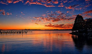 Ein Sonnenuntergang über ruhigem Wasser, mit einem Steg, der sich ins Wasser erstreckt.