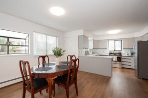 Una cocina moderna con armarios blancos, una mesa de comedor con sillas y un amplio ventanal con persianas.