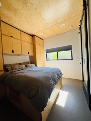 Ein Schlafzimmer mit Bett, Holzschränken, einem Fenster mit Jalousien und einer Decke mit Einbauleuchten.