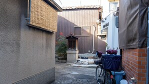 A narrow alleyway with a bicycle parked on the right, a trash bin, and a building with a wooden door. - Korean Town Front/ Sleeps 8/ 9 Min Walk to Tsuruhashi St/ Direct Access to Namba (Osaka)
