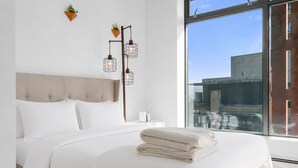 Una camera da letto moderna con un letto grande, un comodino, una lampada e vista sulla città attraverso un'ampia finestra.