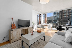A modern living room with a TV, a guitar, a dining table with chairs, and a sofa.