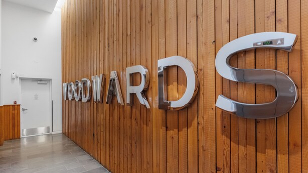 Una parete di legno con le lettere 'WOODWARD' e una grande 'S' metallica in una zona d'ingresso.