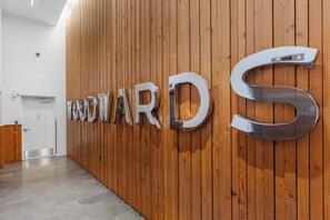 A wooden wall with the letters 'WOODWARD' and a large metallic 'S' in a lobby area. - Woodward's Gastown Condo | Walk to Stadium & Waterfront Views (Vancouver)