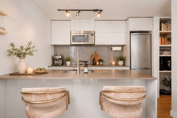 A modern kitchen with a central island, stainless steel appliances, and a minimalist design. - Woodward's Gastown Condo | Walk to Stadium & Waterfront Views (Vancouver)