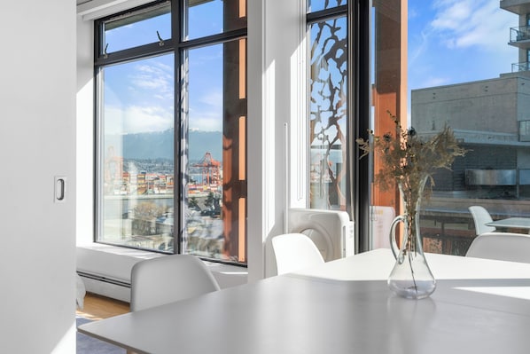 A modern room with large windows, a white table, and a vase with dried flowers.