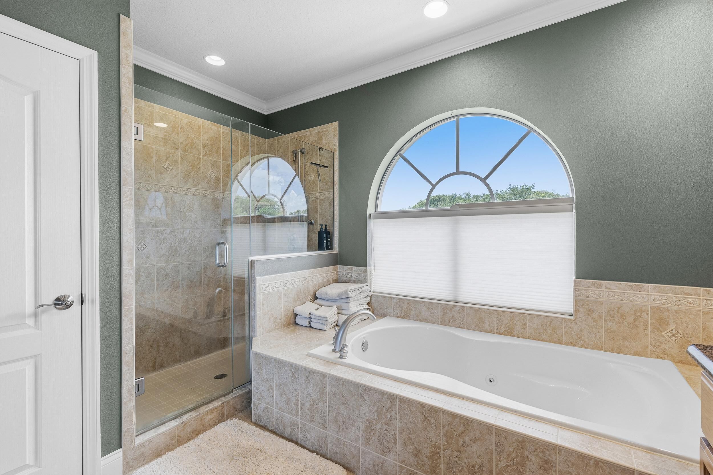 A bathroom with a glass-enclosed shower, a large bathtub, and a window with a view.