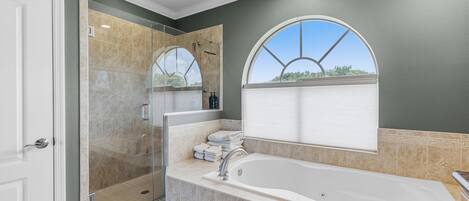 A bathroom with a glass-enclosed shower, a large bathtub, and a window with a view.