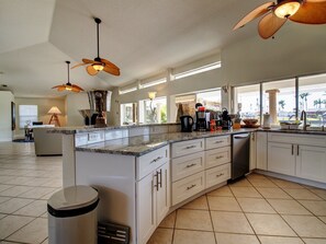 A spacious kitchen with a large island, modern appliances, and large windows offering a view. - Waterpark Style Pool With Hot Tub in Grotto With Waterfall and Bridge Over Pool (Cape Coral)