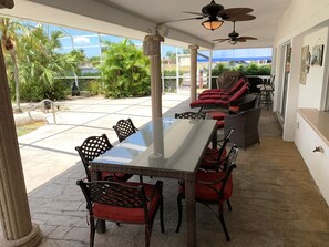 A covered patio with a glass table, wicker chairs, and a ceiling fan. - Waterpark Style Pool With Hot Tub in Grotto With Waterfall and Bridge Over Pool (Cape Coral)