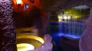 An indoor hot spring area with a waterfall, stone walls, and a small window. - Waterpark Style Pool With Hot Tub in Grotto With Waterfall and Bridge Over Pool (Cape Coral)
