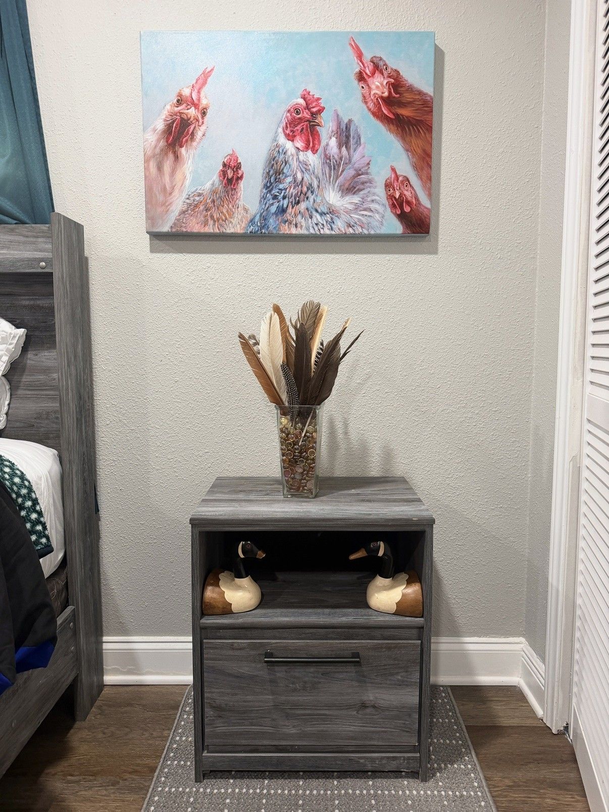A room with a bed, a nightstand with a vase, and a painting on the wall.
