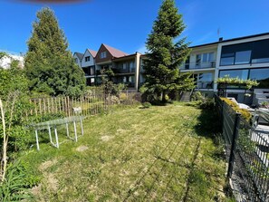Un barrio residencial con césped, una valla metálica y edificios de varios pisos al fondo.
