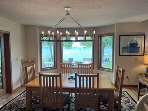 A dining area with a table and chairs, large windows with a view of the water, and a chandelier.