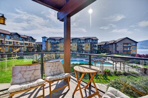 Un balcon agrémenté de deux fauteuils confortables et d’une petite table, donnant sur une piscine et un jardin aménagé.