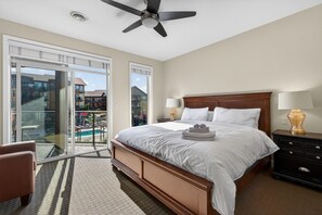Une chambre d’hôtel avec un grand lit, un ventilateur de plafond, un balcon donnant sur la piscine et une table de chevet avec des lampes.