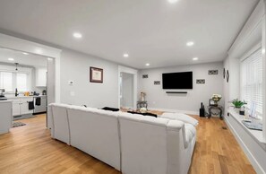 Una sala de estar moderna con un sofá, un televisor de pantalla plana y un comedor con una cocina al fondo.