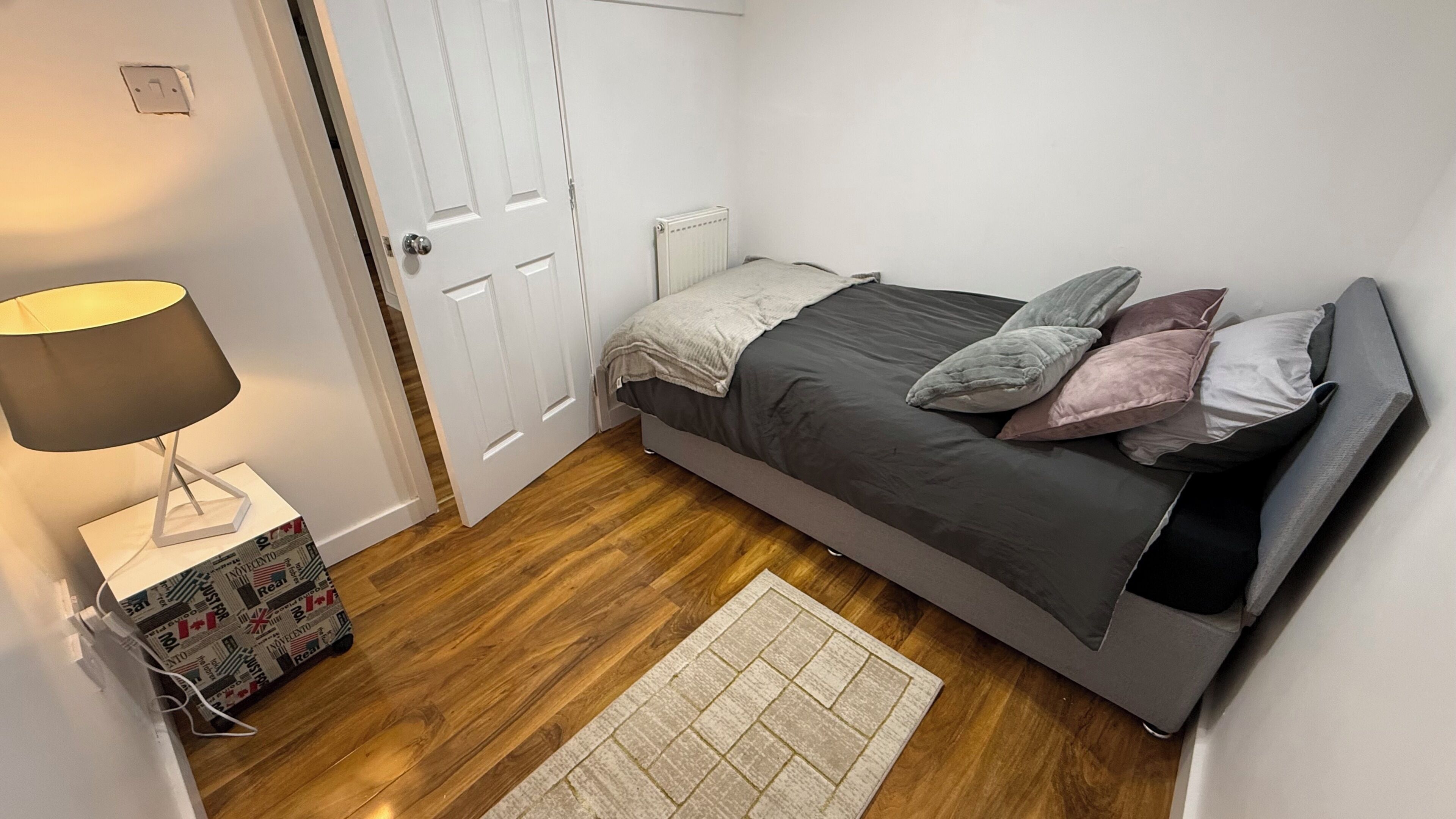Une petite chambre à coucher, bien rangée, avec un lit, une lampe de chevet, un radiateur et un tapis.