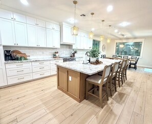 A spacious kitchen with white cabinets, a large island, and pendant lighting.