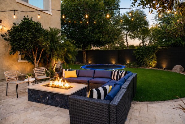 An outdoor patio with a fire pit, a sofa, and a trampoline.