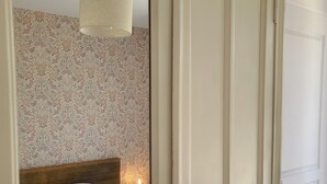 A bedroom with a bed, a nightstand with a candle, and a mirror reflecting the room. - Charming town house, 10min walk to the beach (saint gildas de rhuys)