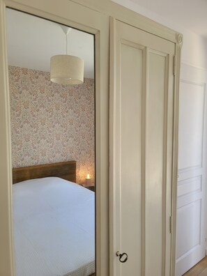 A bedroom with a bed, a nightstand with a candle, and a mirror reflecting the room. - Charming town house, 10min walk to the beach (saint gildas de rhuys)