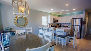 Une cuisine moderne avec des meubles blancs, un réfrigérateur en acier inoxydable et un coin repas comprenant une table en bois et des chaises blanches.