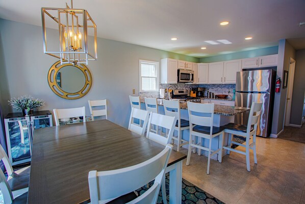 A modern kitchen with white cabinets, a stainless steel refrigerator, and a dining area with a wooden table and white chairs.
