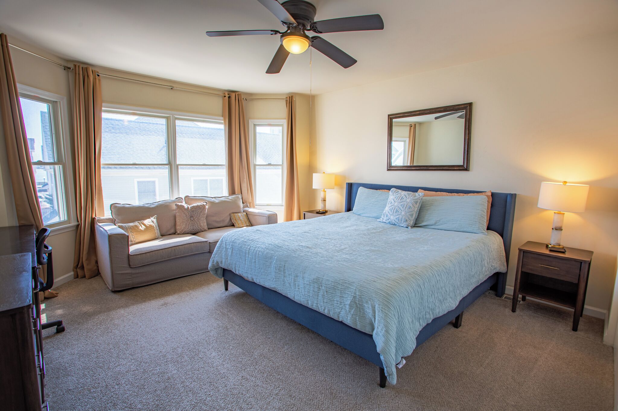A bedroom with a bed, a sofa, a ceiling fan, a nightstand, and a window.