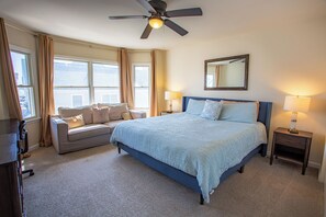A bedroom with a bed, a sofa, a ceiling fan, a nightstand, and a window.