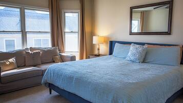 A bedroom with a bed, a sofa, a lamp, a mirror, and windows.