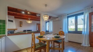 A dining area with a wooden table, chairs, a chandelier, and a view through large windows. - Pet-Friendly Family House with Garden near Piešťany Spa Town (Brunovce)