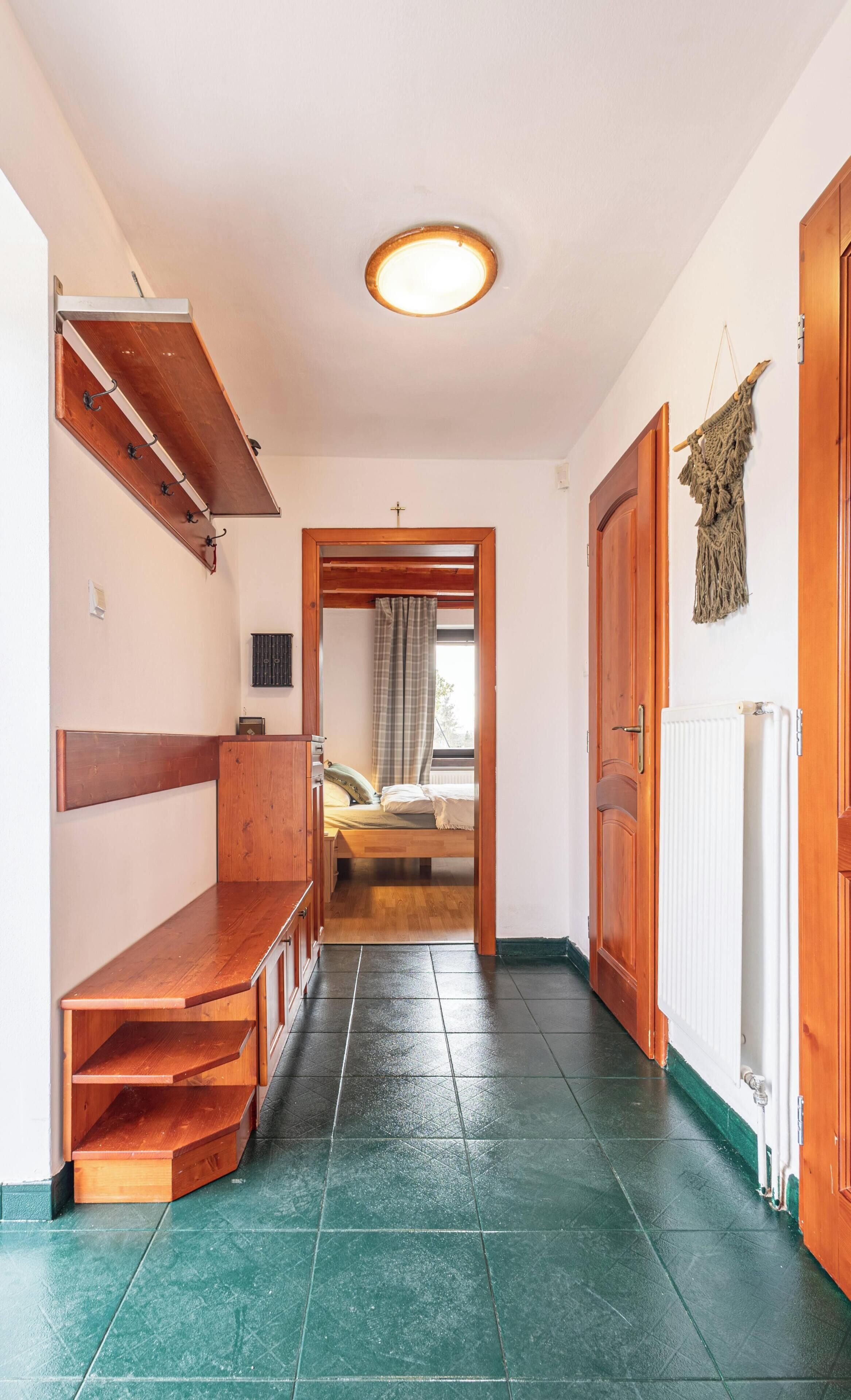 Een gang die leidt naar een slaapkamer met een bed, een radiator en een houten bank.