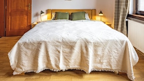 A bedroom with a wooden ceiling, a bed with a white quilt, a headboard, a bedside lamp, and a window with curtains. - Pet-Friendly Family House with Garden near Piešťany Spa Town (Brunovce)