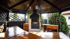 A covered outdoor area with a wooden table, a grill, and a lantern. - Pet-Friendly Family House with Garden near Piešťany Spa Town (Brunovce)