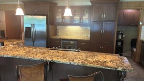 Una cocina con encimeras de granito, electrodomésticos de acero inoxidable, gabinetes de madera e iluminación colgante.
