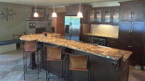 Una cocina con encimera de granito, armarios de madera oscura, refrigerador de acero inoxidable e iluminación colgante.
