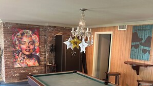 Una mesa de billar en una habitación con pared de ladrillo, una araña y un cartel en la pared.