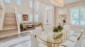 A spacious living area with a glass dining table, a staircase, and a large chandelier. - Elegant 5BR Gem @Ontario w/ Grill | Near Airport (Ontario)
