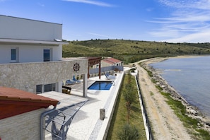 Ein modernes Gebäude mit Pool, Blick auf das Meer und einer hügeligen Landschaft im Hintergrund.