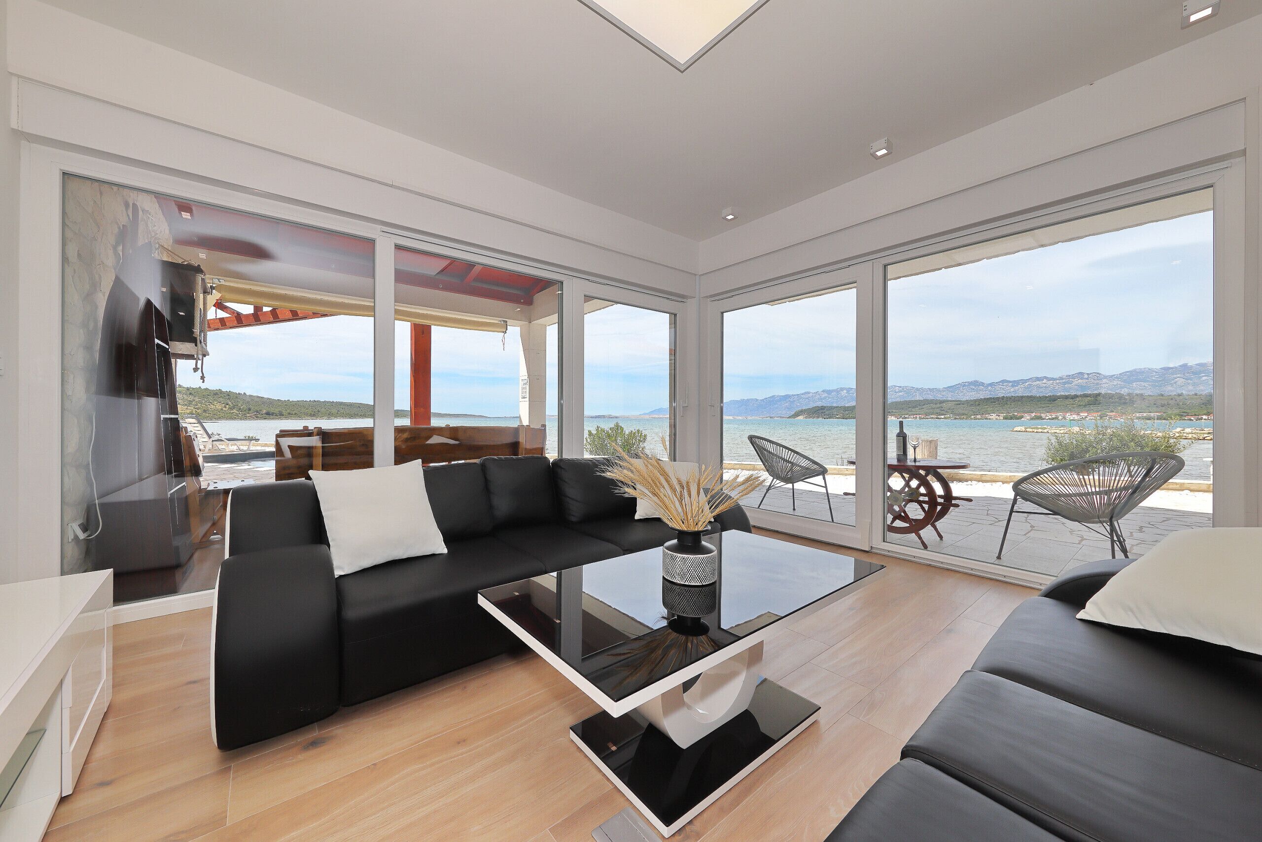 Ein modernes Wohnzimmer mit einer schwarzen Couch, einem Glastisch und Meerblick durch große Fenster.