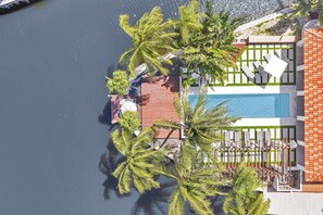 Ovenfra ses et resort med en swimmingpool, palmer og et afspærret område med liggestole.