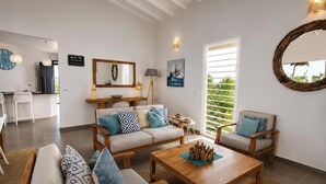 A living room with a sofa, coffee table, and chairs, a dining area with a table and chairs, a large mirror, and a window with blinds. - Villa Ouassou, sea view and swimming pool between Gosier and St Anne (st anne)