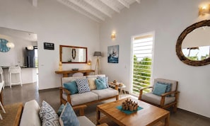 A living room with a sofa, coffee table, and chairs, a dining area with a table and chairs, a large mirror, and a window with blinds. - Villa Ouassou, sea view and swimming pool between Gosier and St Anne (st anne)
