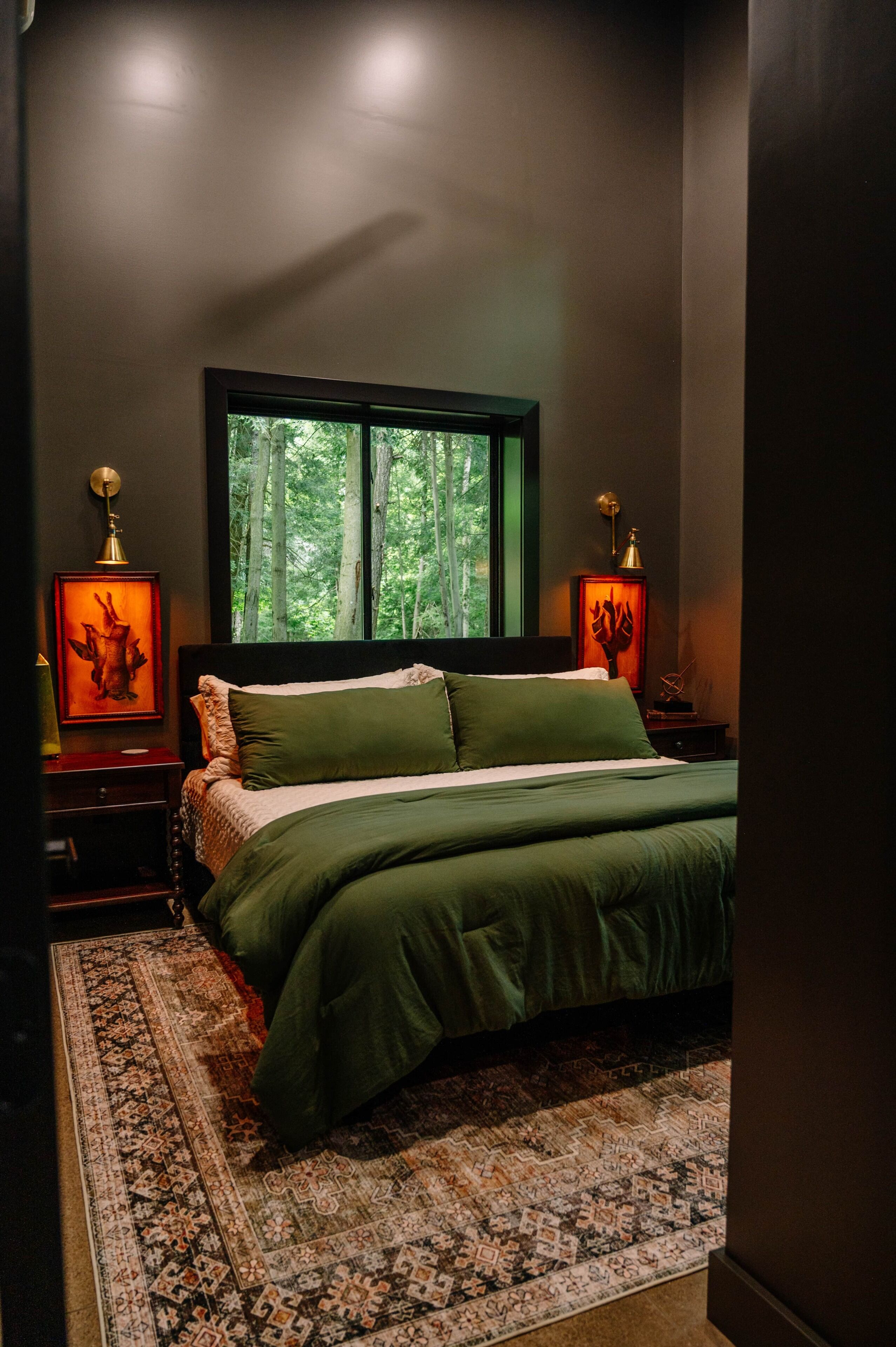 A bedroom with a large bed, a window with a view of trees, and two bedside lamps.