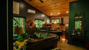 Uma sala de estar aconchegante com um sofá de couro, uma área de jantar com parede de tijolos e uma cozinha com luminária pendente.