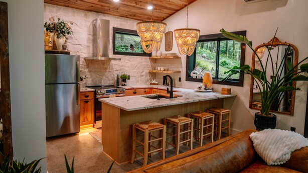 Uma cozinha com ilha central, banquetas, teto de madeira e janelas amplas.