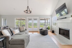 A spacious living room with a large sectional sofa, a fireplace, and a television mounted on the wall. - Cozy Lakefront Retreat. Family Friendly w/ Kayaks, Pool Access, Pickleball! (Spicewood)