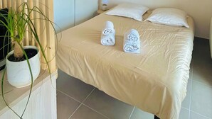 A neatly made bed with two rolled towels, a potted plant, and a hanging light fixture in a room with a minimalist design. - T1 bis - Quiet in La Rochelle (La Rochelle)